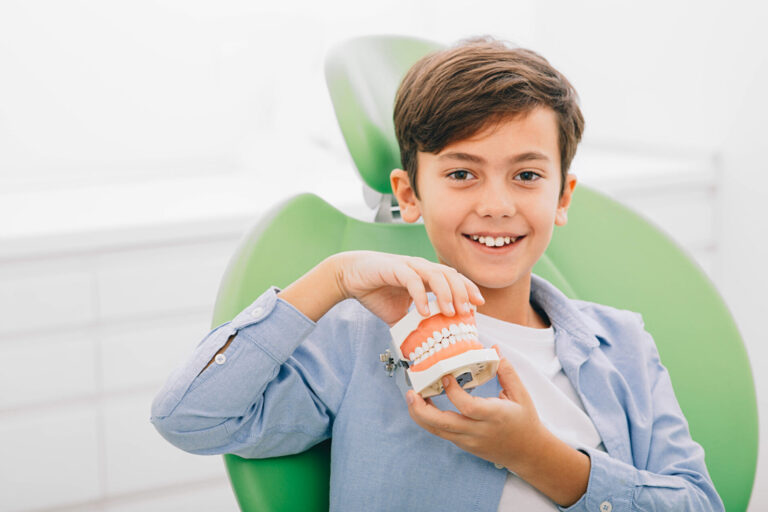 Mixed-race boy holding dental jaw while sitting in dental chair. He is happy after teeth treatment